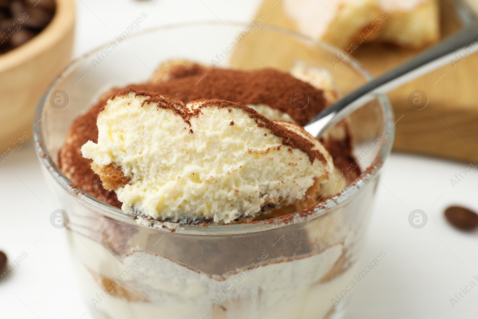 Photo of Delicious tiramisu in glass and spoon on white table, closeup