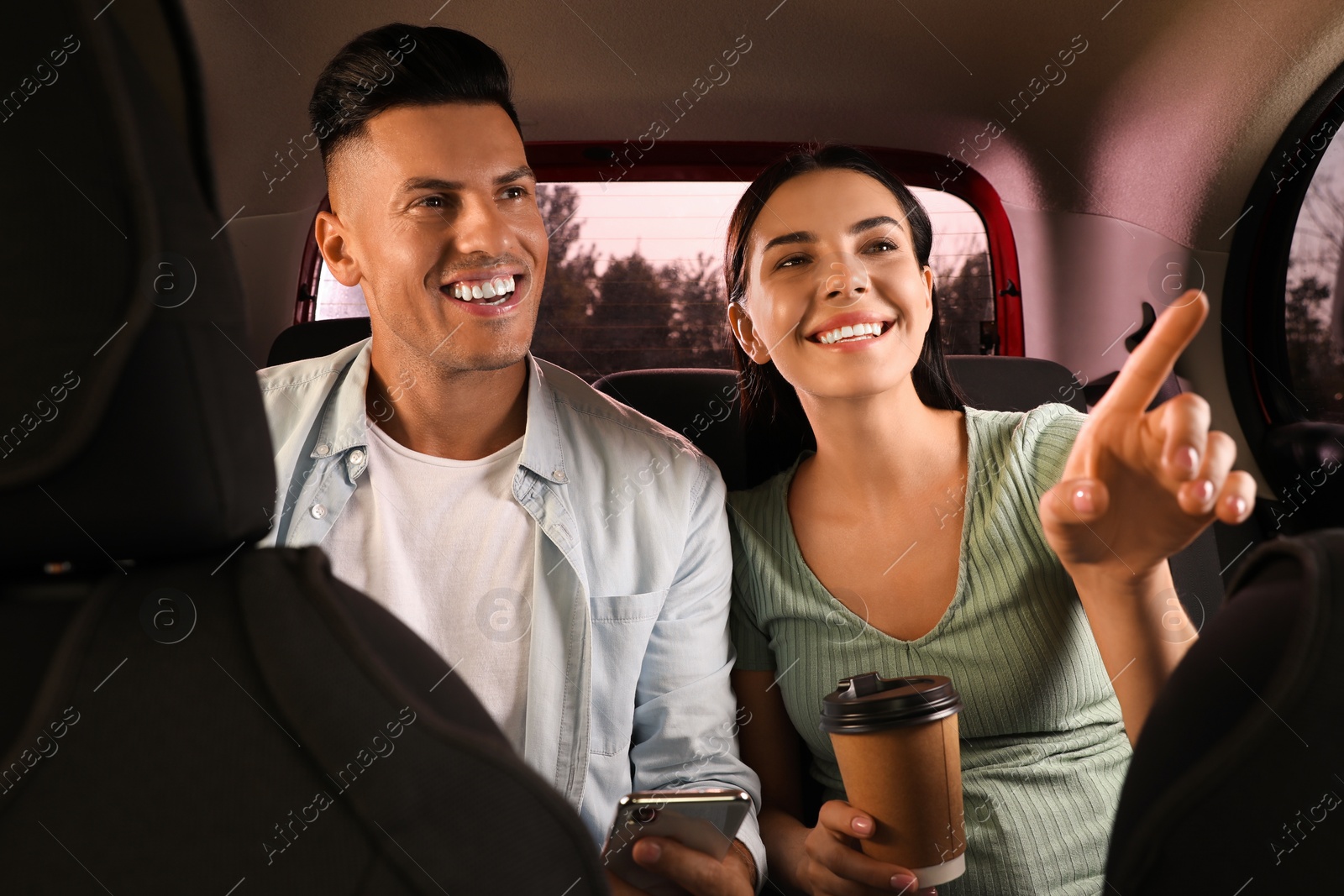 Photo of Happy couple with smartphone and cup of drink in modern taxi