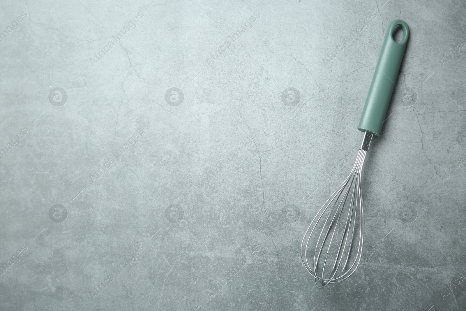 Photo of Metal whisk on gray table, top view. Space for text