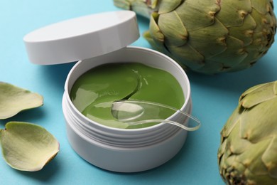 Photo of Package of under eye patches and artichokes on light blue background, closeup. Cosmetic product