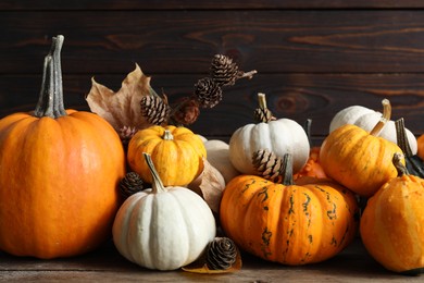 Photo of Thanksgiving day. Composition with pumpkins, leaves and conifer cones on wooden table, closeup