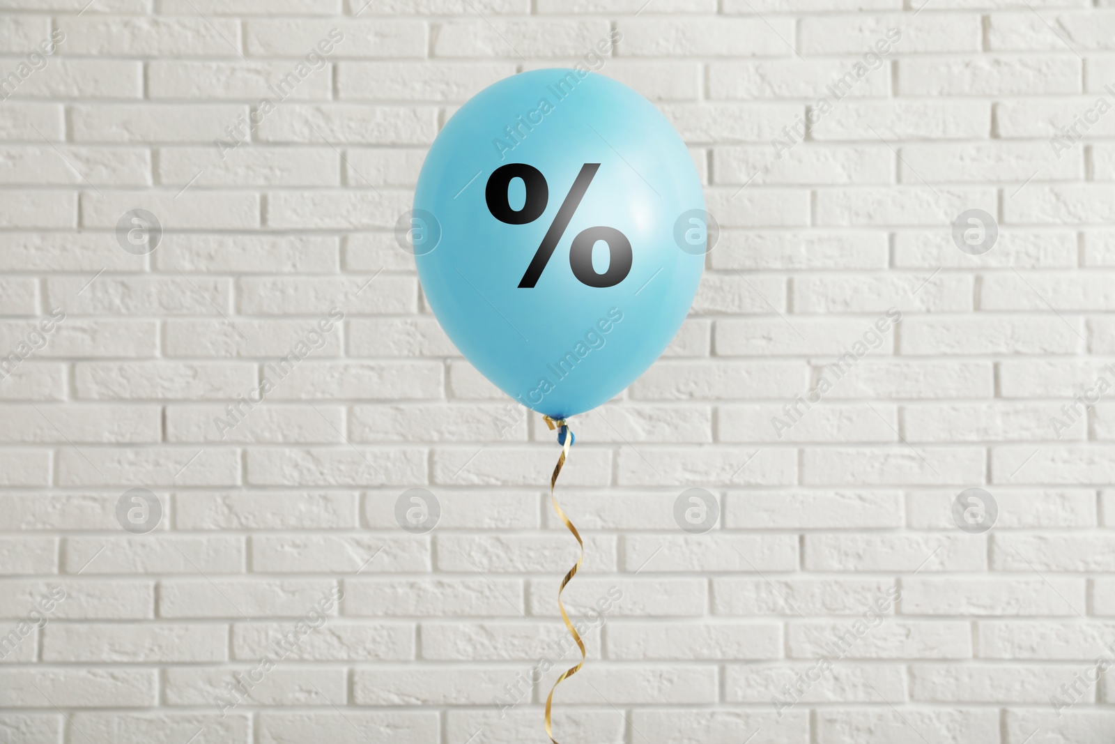 Image of Discount offer. Light blue balloon with percent sign against white brick wall