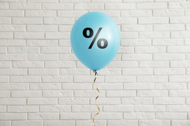 Image of Discount offer. Light blue balloon with percent sign against white brick wall