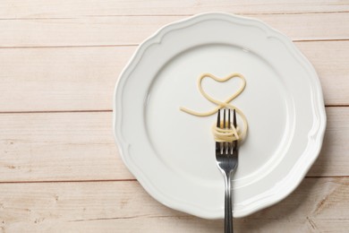 Photo of Heart made of tasty spaghetti and fork on wooden table, top view. Space for text