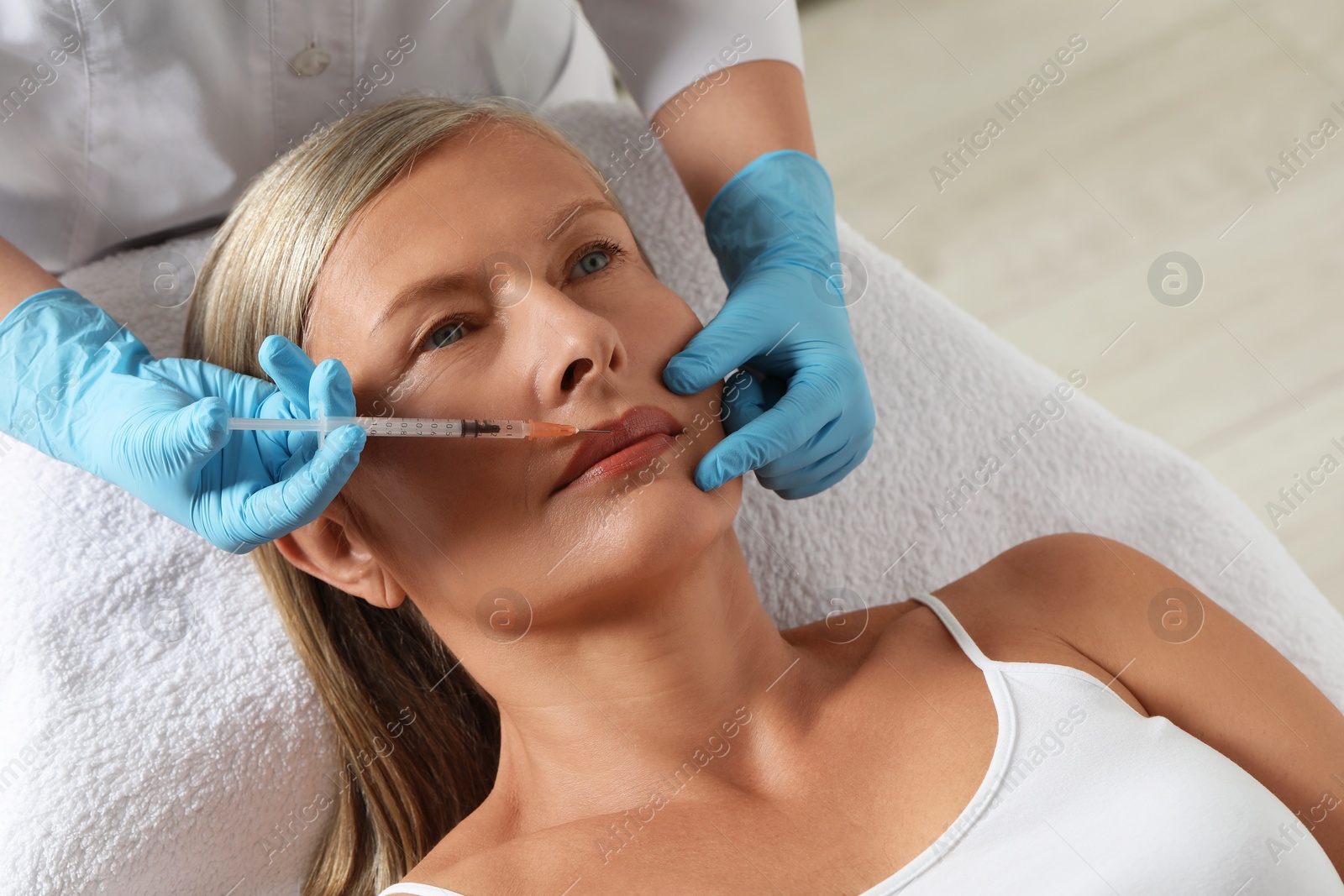 Photo of Doctor giving lips injection to senior woman in clinic. Cosmetic surgery