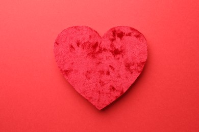 One velvet heart on red background, top view