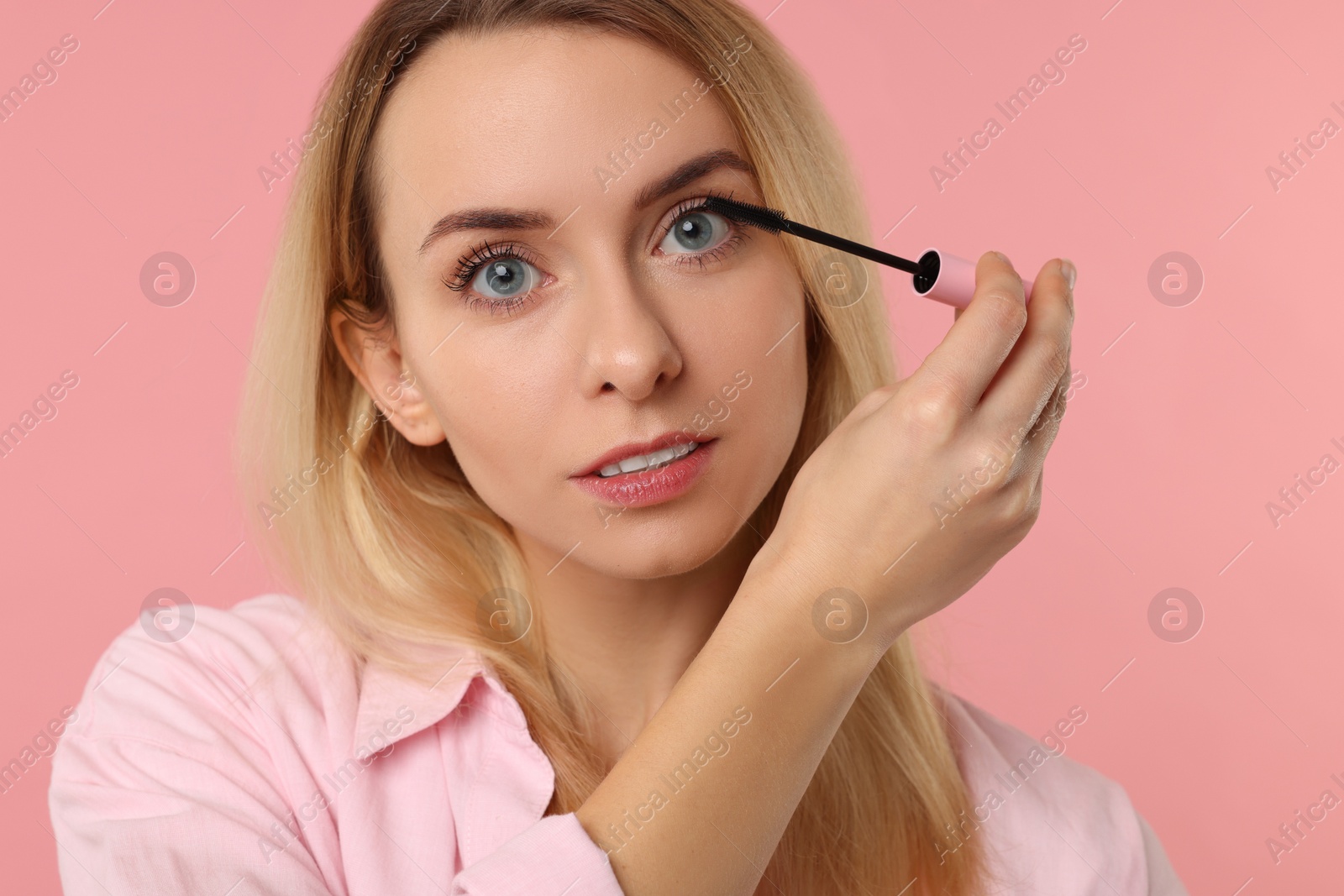 Photo of Beautiful woman applying mascara on pink background, closeup