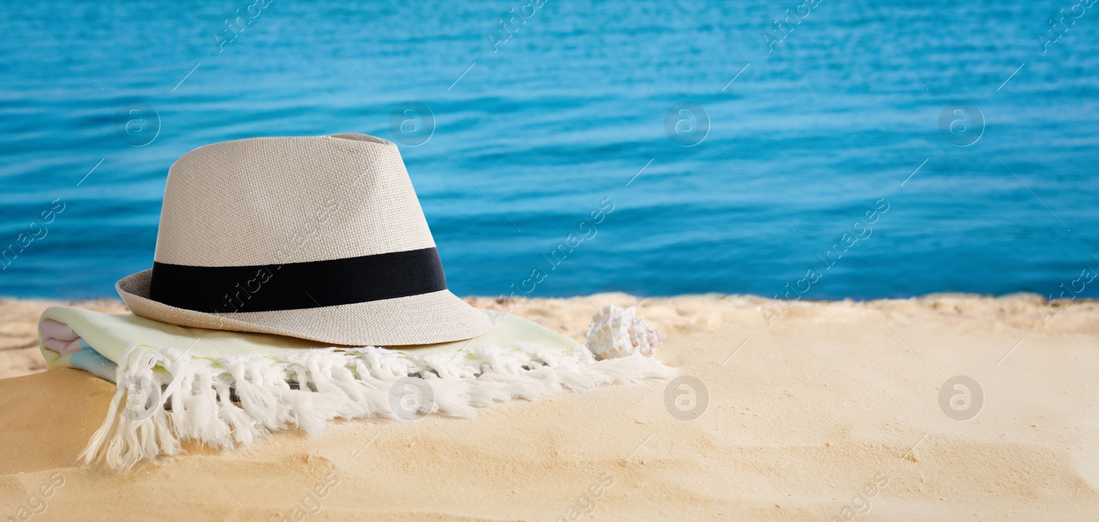 Image of Hat and towel on sandy beach near sea, space for text. Summer vacation 