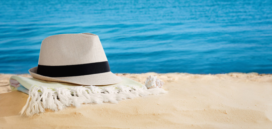 Hat and towel on sandy beach near sea, space for text. Summer vacation 