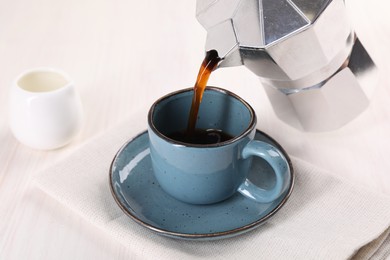 Photo of Pouring aromatic coffee from moka pot into cup at white wooden table, closeup