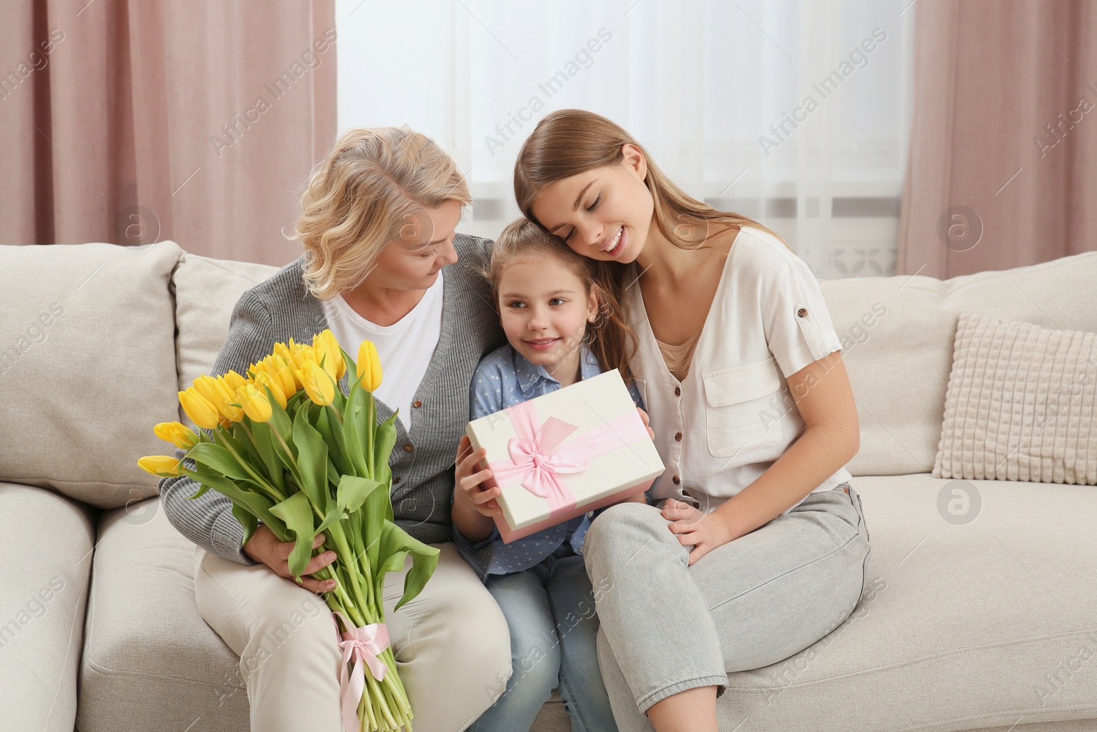 Photo of Little girl congratulating her mom and granny with flowers and gift at home. Happy Mother's Day