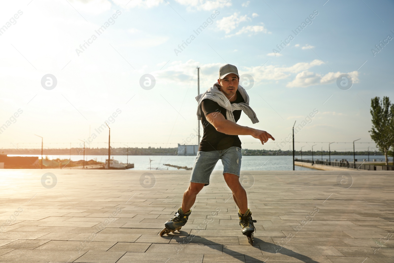 Photo of Handsome young man roller skating on pier near river, space for text