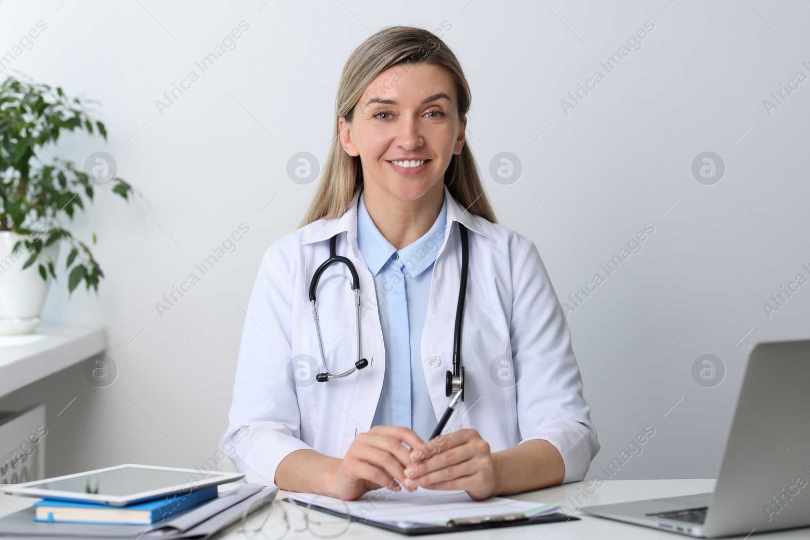 Photo of Portrait of happy doctor with stethoscope at white table in hospital