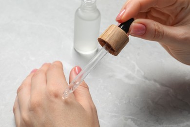 Photo of Woman dripping serum from pipette on her hand at light grey marble table, closeup