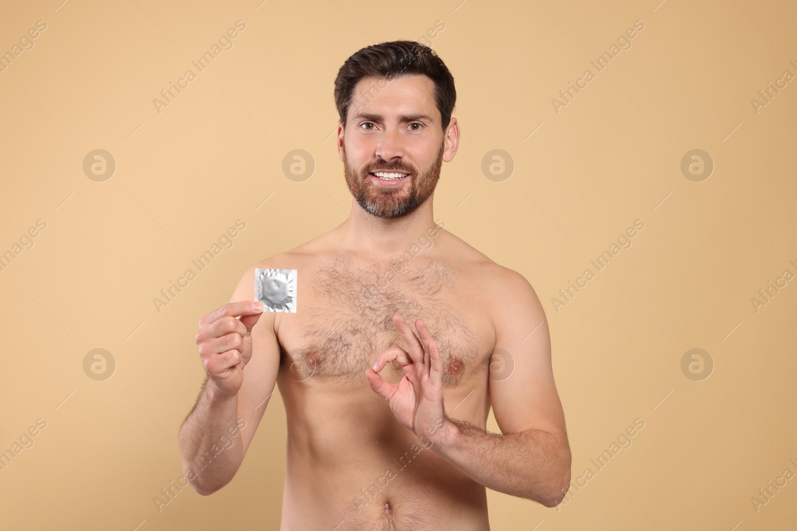Photo of Naked man with condom showing ok gesture on beige background. Safe sex