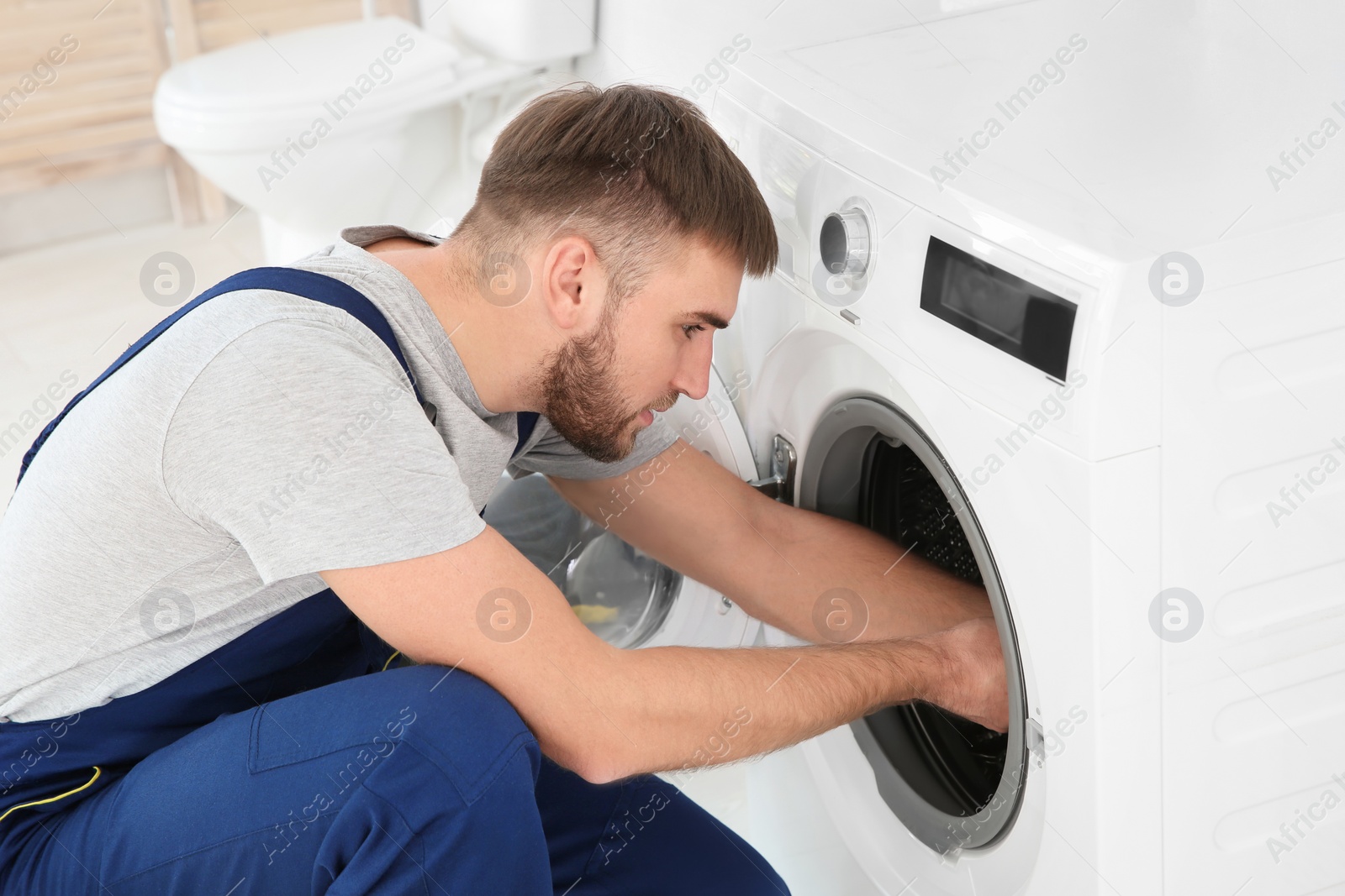 Photo of Young plumber fixing washing machine in bathroom