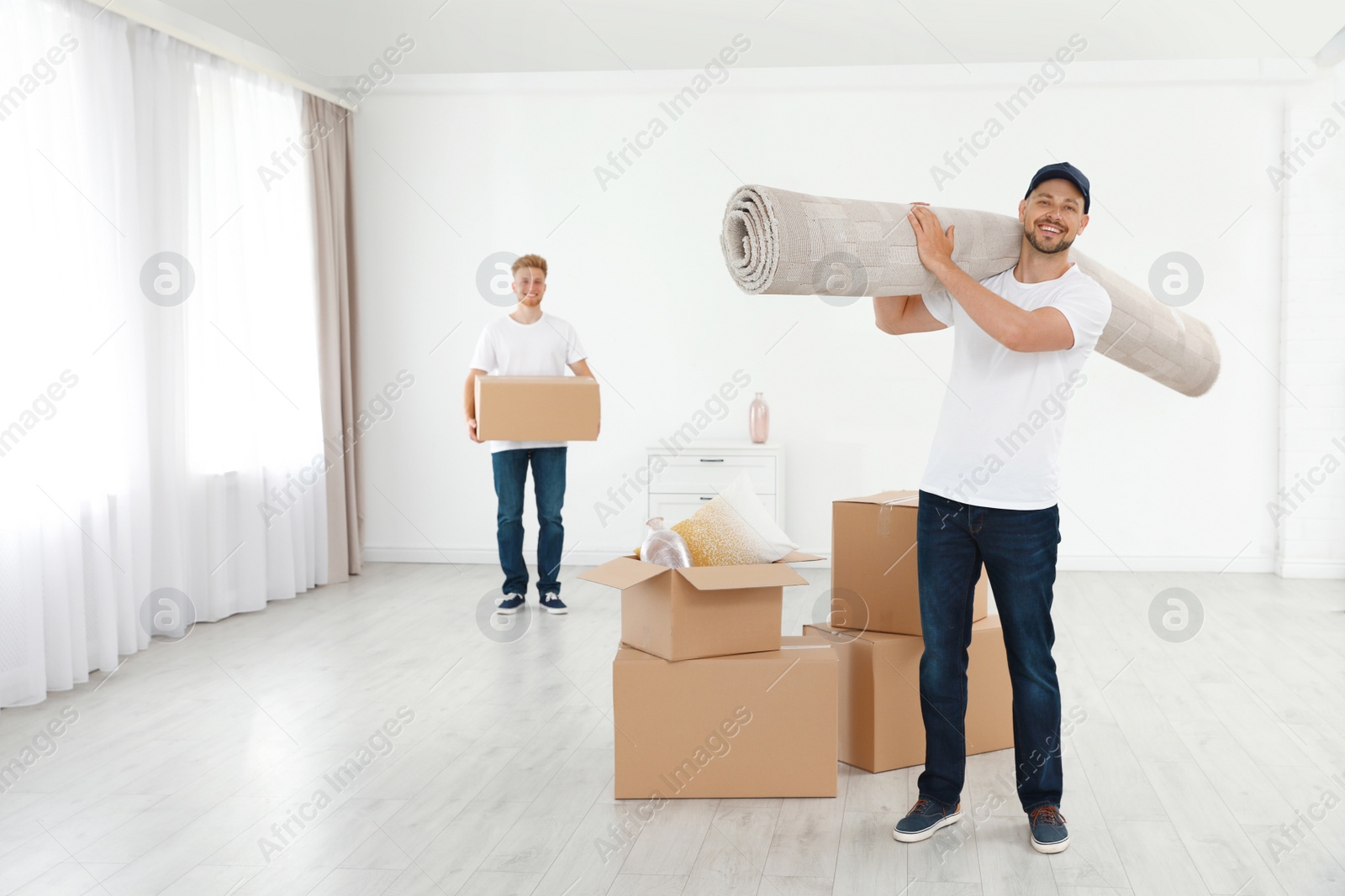 Photo of Moving service employees with cardboard boxes and carpet in room