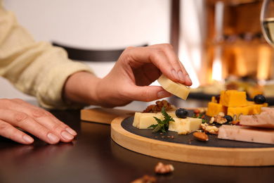 Photo of Woman taking piece of delicious cheese at table indoors, closeup