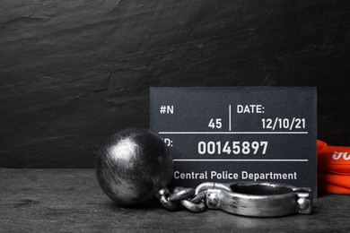 Metal ball with chain, prison uniform and mugshot letter board on grey table