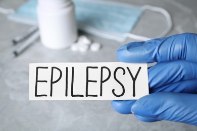 Photo of Doctor holding card with word Epilepsy at grey table, closeup