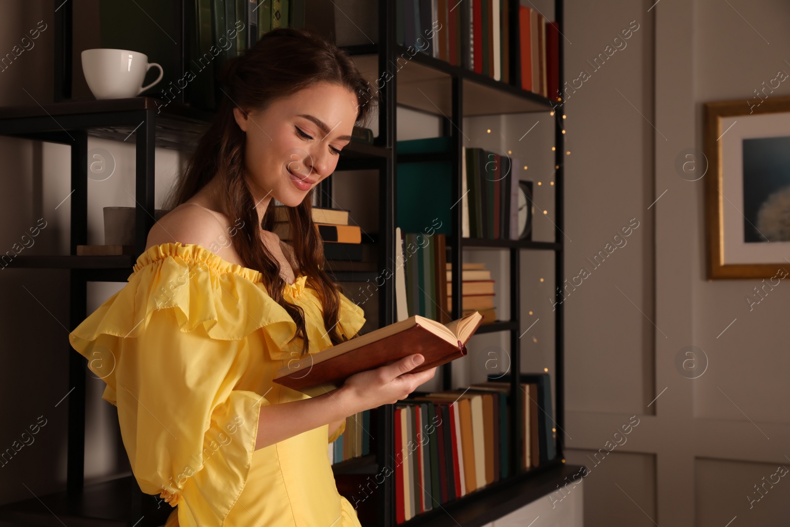 Photo of Beautiful young woman in yellow dress reading book at home