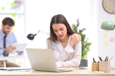 Young woman suffering from shoulder pain in office