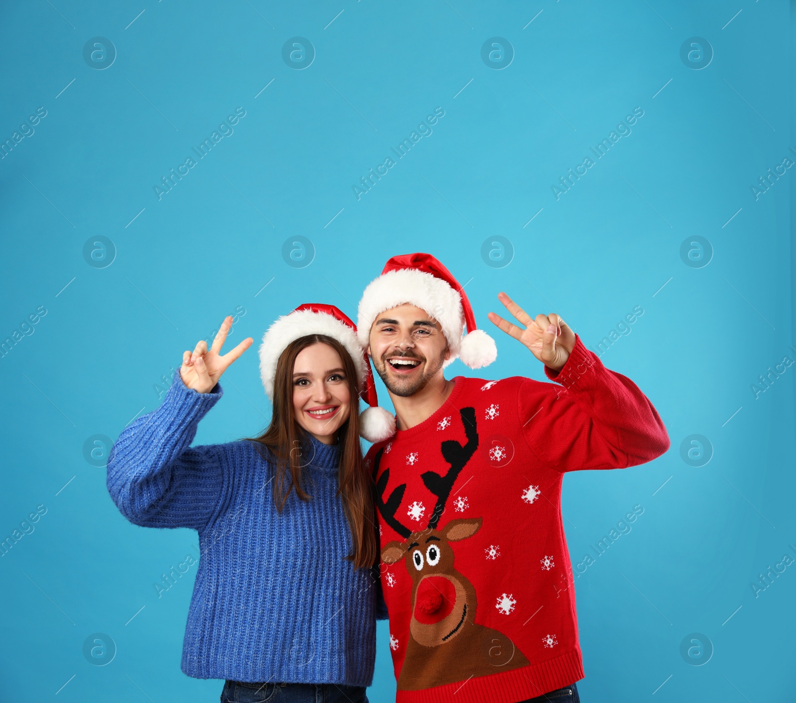 Photo of Couple wearing Christmas sweaters and Santa hats on blue background