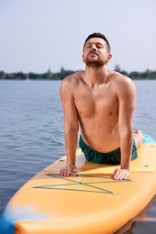 Man practicing yoga on SUP board on river