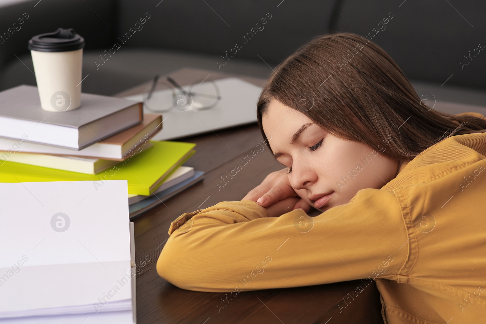 Photo of Young tired woman sleeping near books at wooden table indoors