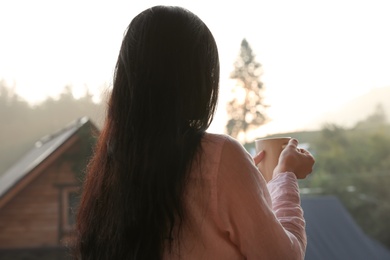 Young woman with cup of tea enjoying beautiful view in morning