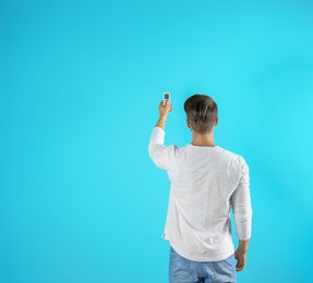 Young man with air conditioner remote on color background