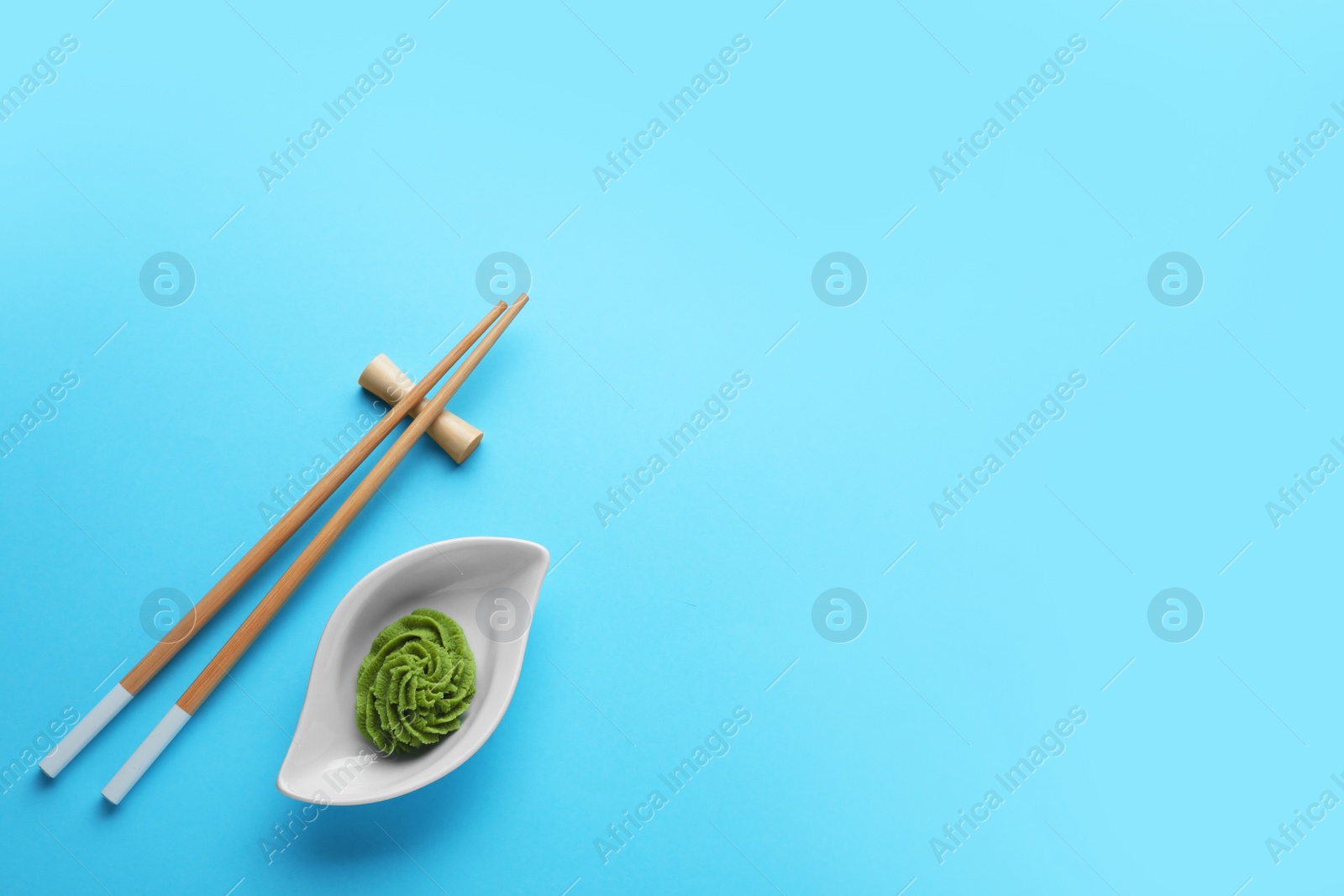 Photo of Bowl with swirl of wasabi paste and chopsticks on light blue background, flat lay. Space for text