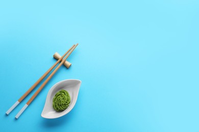 Photo of Bowl with swirl of wasabi paste and chopsticks on light blue background, flat lay. Space for text