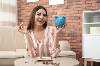 Photo of Happy young woman with piggy bank and money at home