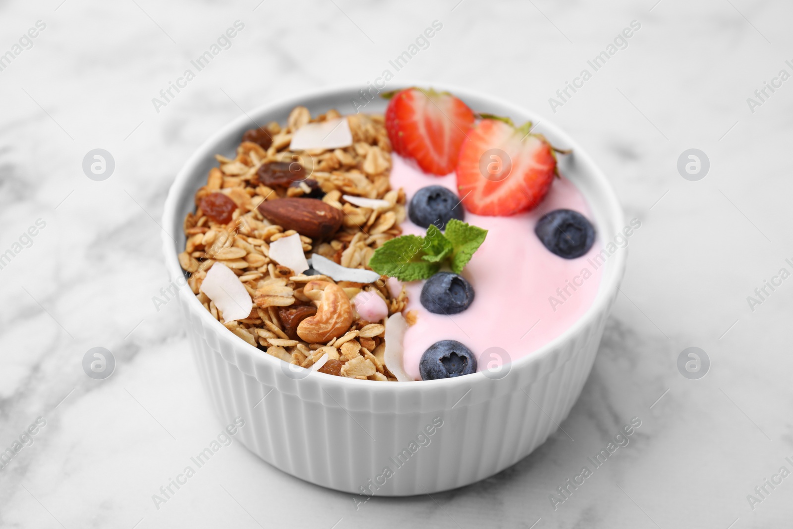 Photo of Tasty granola, yogurt and fresh berries in bowl on white marble table, closeup. Healthy breakfast