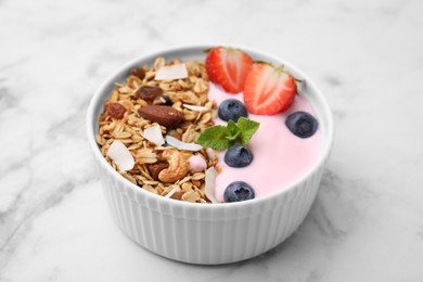 Tasty granola, yogurt and fresh berries in bowl on white marble table, closeup. Healthy breakfast