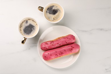 Tasty glazed eclairs and cups of coffee on white marble table, flat lay