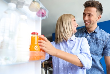 Photo of Couple taking bottle with juice out of refrigerator in kitchen