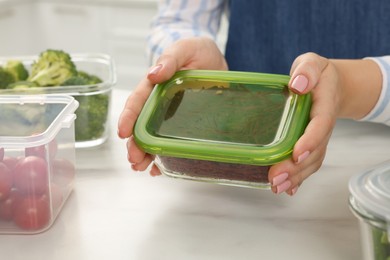 Woman holding glass container with cut fresh red beets at white marble table in kitchen, closeup. Food storage