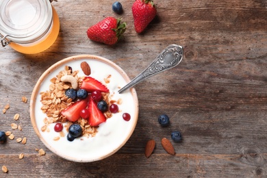 Photo of Tasty breakfast with yogurt, berries and granola on wooden table, top view