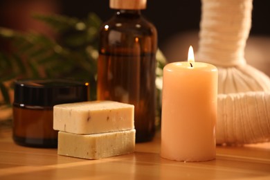 Spa composition. Cosmetic products, herbal bags and burning candle on wooden table, closeup