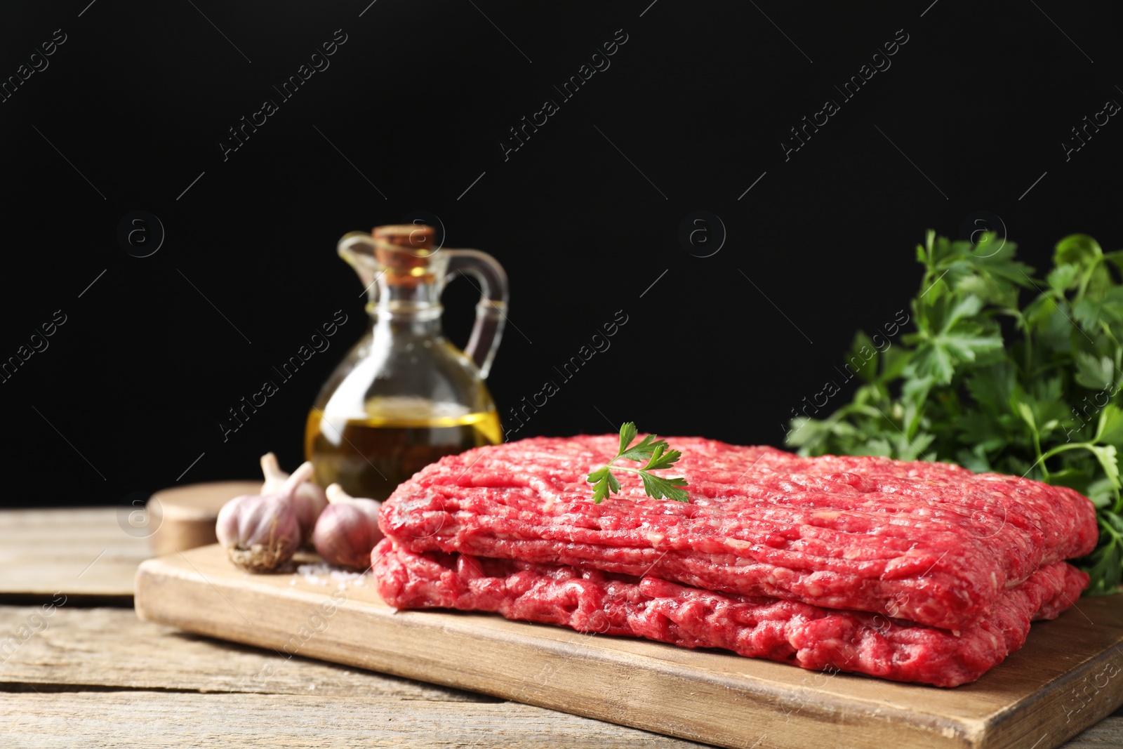 Photo of Raw ground meat, garlic, oil and parsley on wooden table