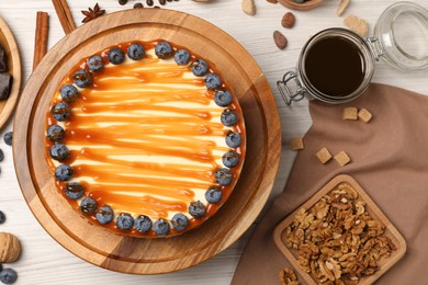 Delicious cheesecake with caramel and blueberries on white wooden table, flat lay