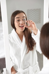 Photo of Attractive young woman curling her eyelashes near mirror indoors