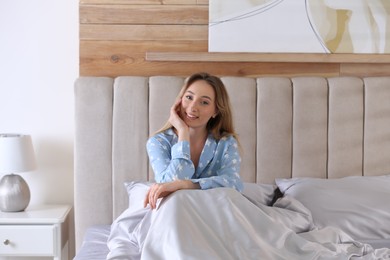 Photo of Young woman sitting on comfortable bed with silky linens