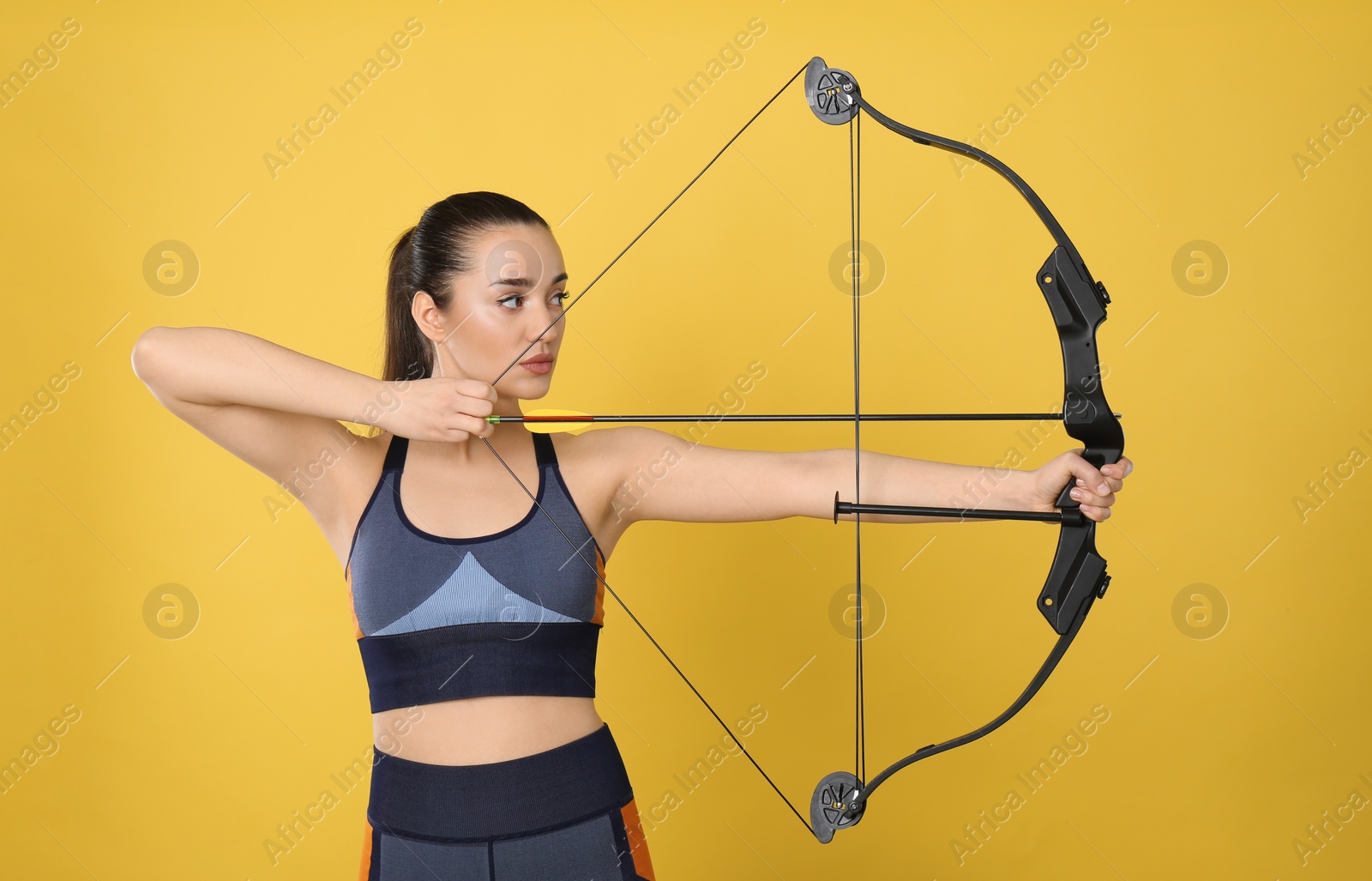 Photo of Sporty young woman practicing archery on yellow background