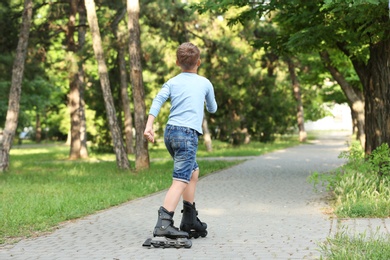 Photo of Little boy roller skating in park, back view