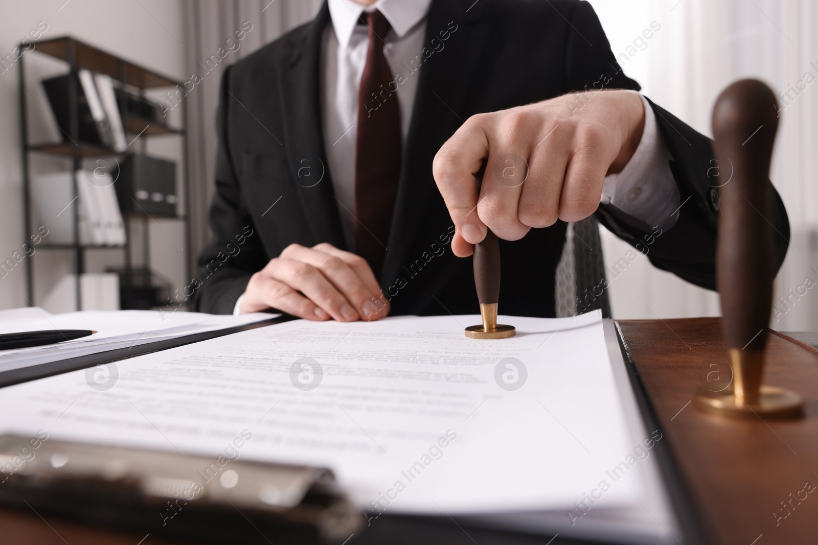 Photo of Notary stamping document at wooden table in office, closeup