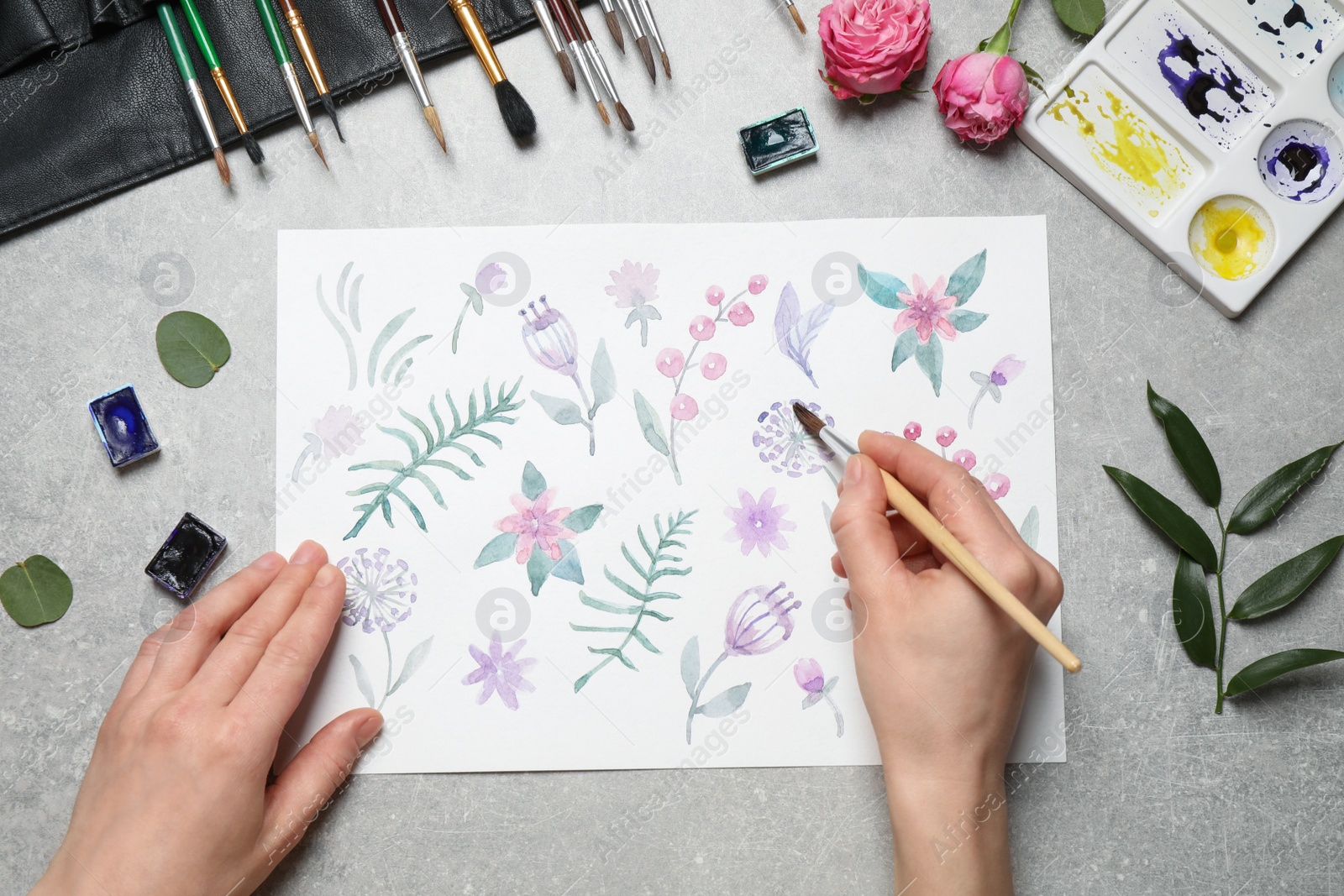 Photo of Woman painting flowers with watercolor at grey stone table, top view