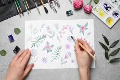 Woman painting flowers with watercolor at grey stone table, top view